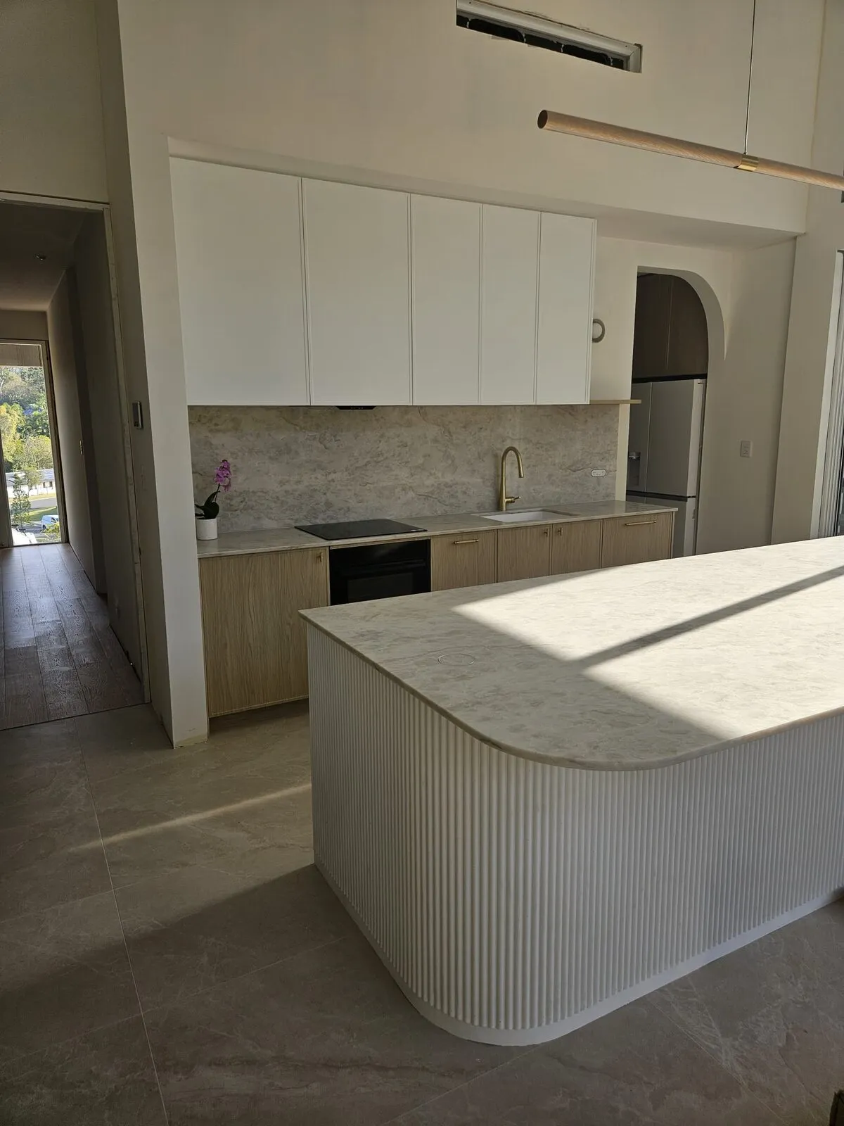 Curved fluted kitchen island with a stone benchtop, looking through to the cabinetry run behind