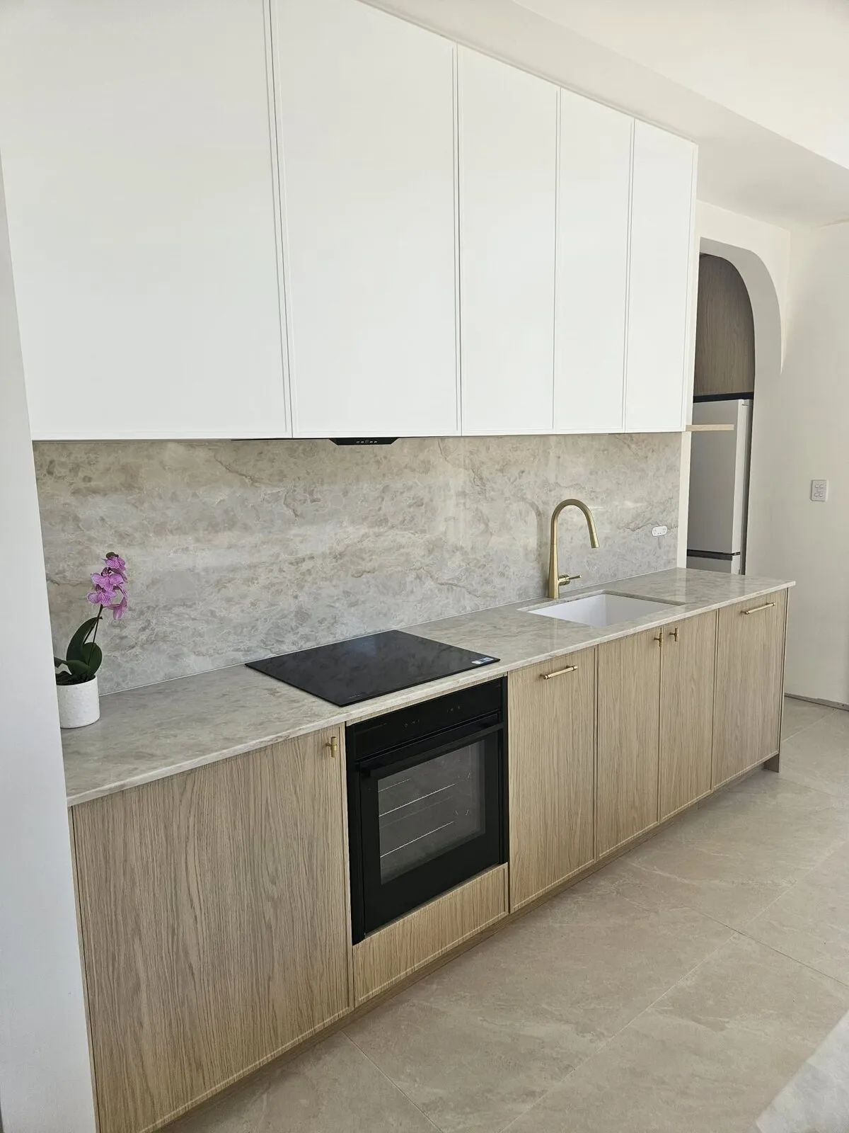 Kitchen run with cooktop, wall oven, sink and stone splashback under handleless overhead cabinets