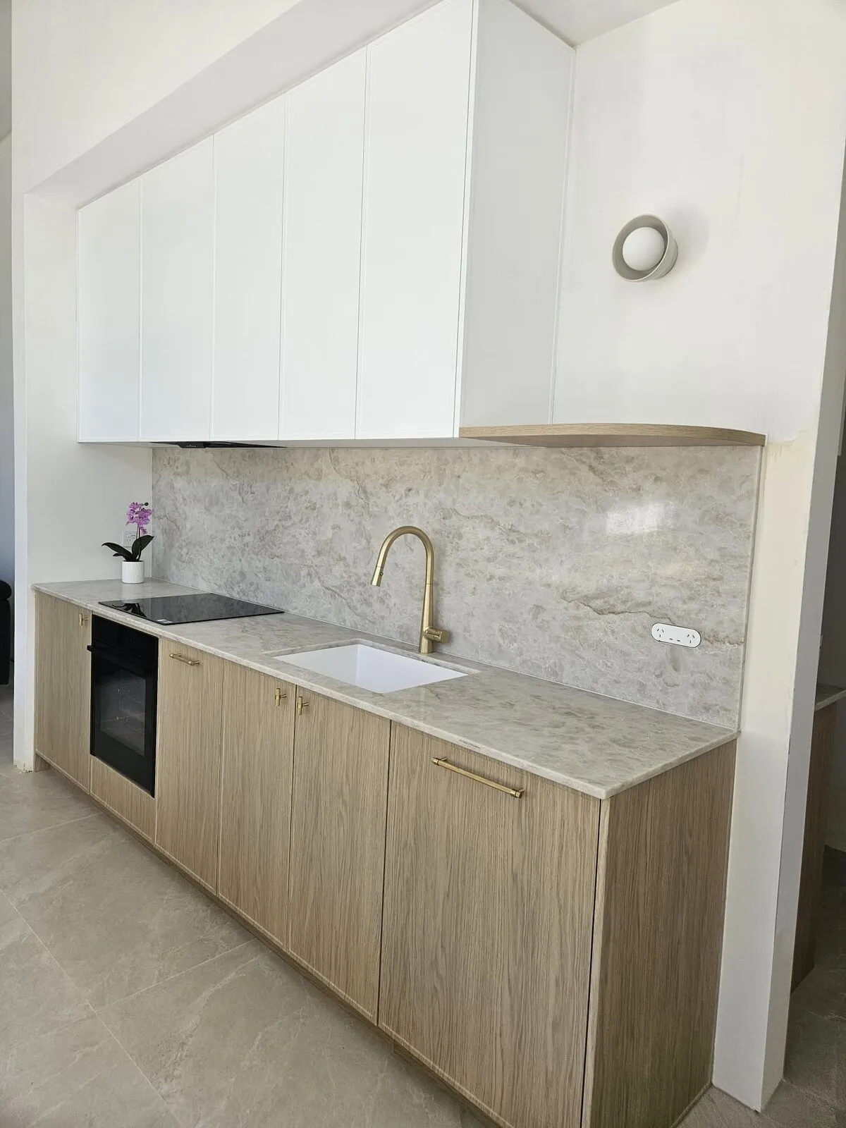 Brushed gold tapware over an undermount sink in a stone benchtop, beside timber cabinetry
