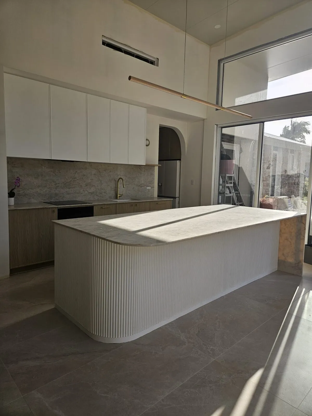 Curved fluted kitchen island with a stone benchtop in Highland Park, timber cabinetry and stone splashback behind