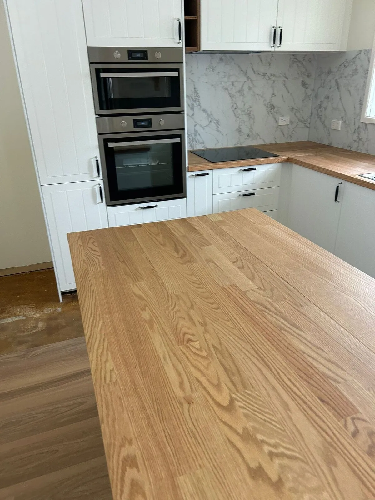 Close view of a solid timber kitchen benchtop showing the grain and the finished edge, with the oven stack behind