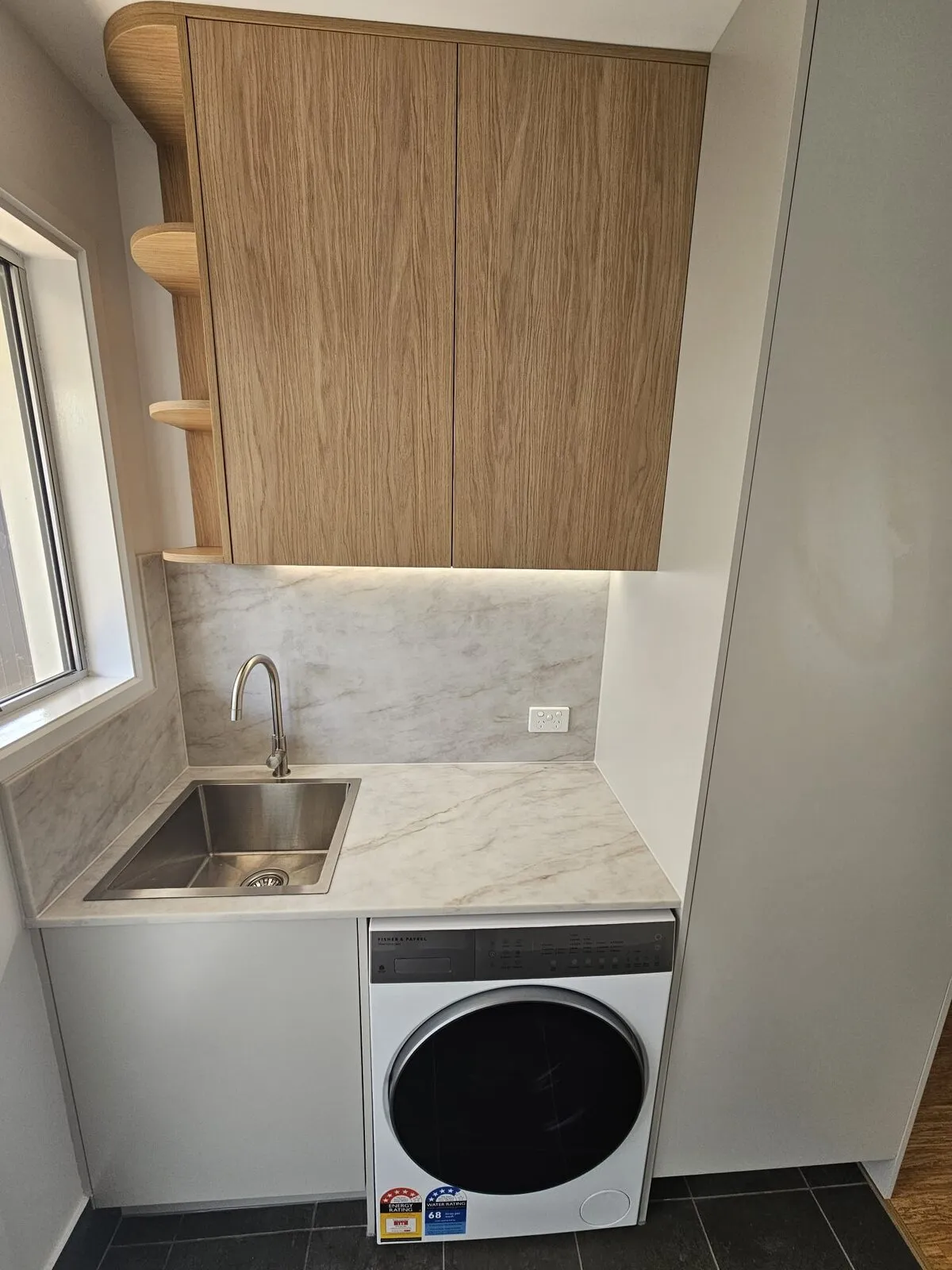 Laundry with timber overhead cupboards, curved open end shelves, stone splashback and an undermount trough beside a washing machine