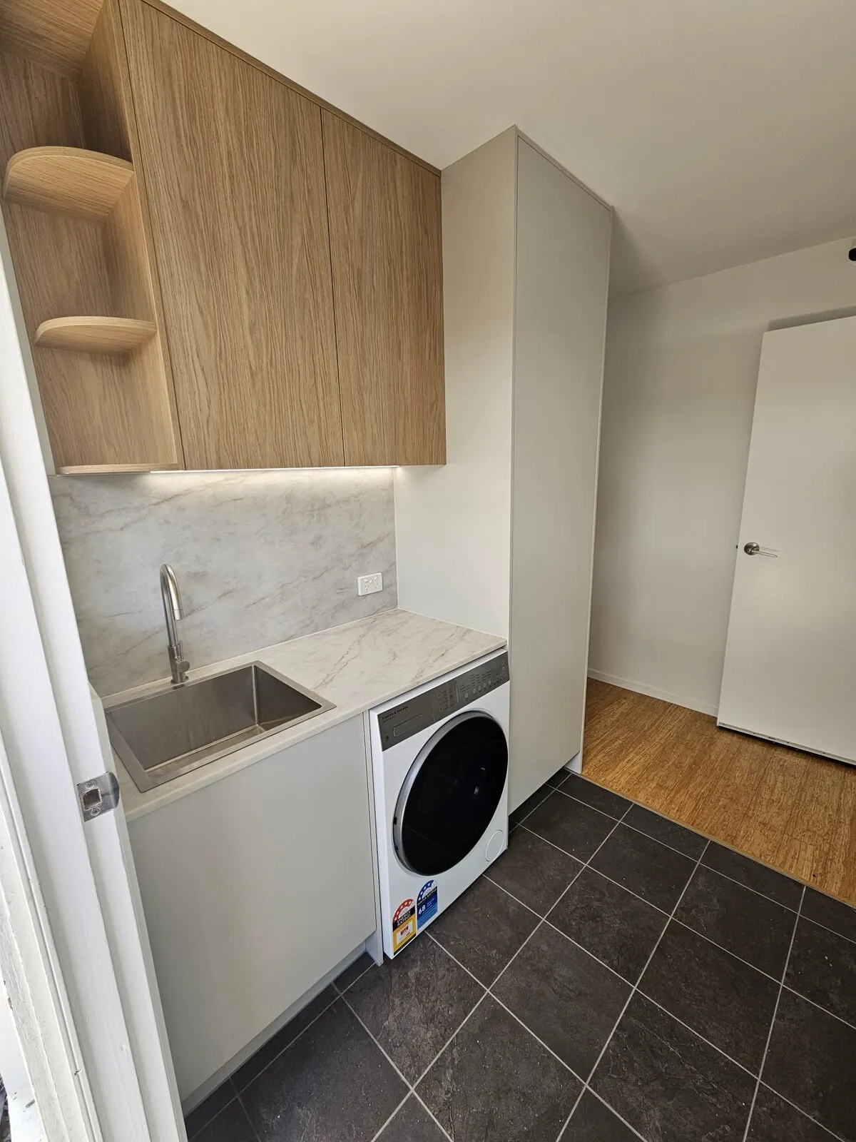 Stone benchtop and splashback with a stainless trough and gooseneck mixer, the bench continuing over the washing machine