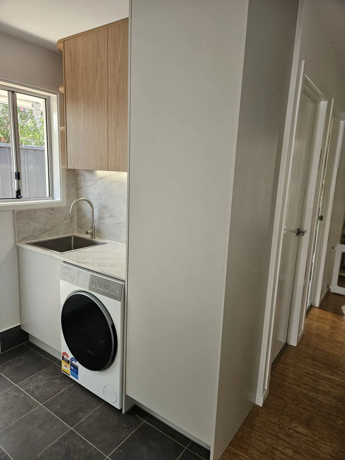 The finished laundry seen from the doorway, tall white cupboard to one side and dark tiled floor
